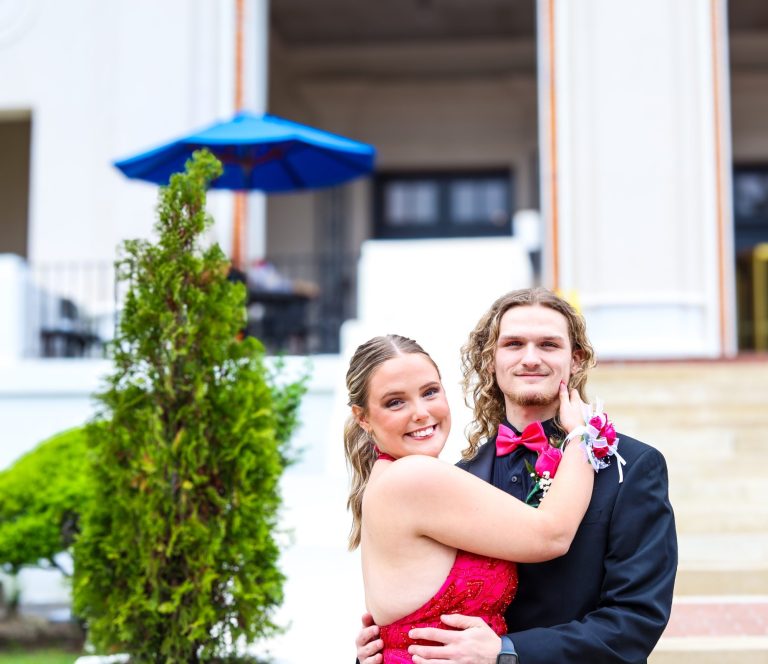 A couple poses together, smiling, dressed elegantly for a formal event.