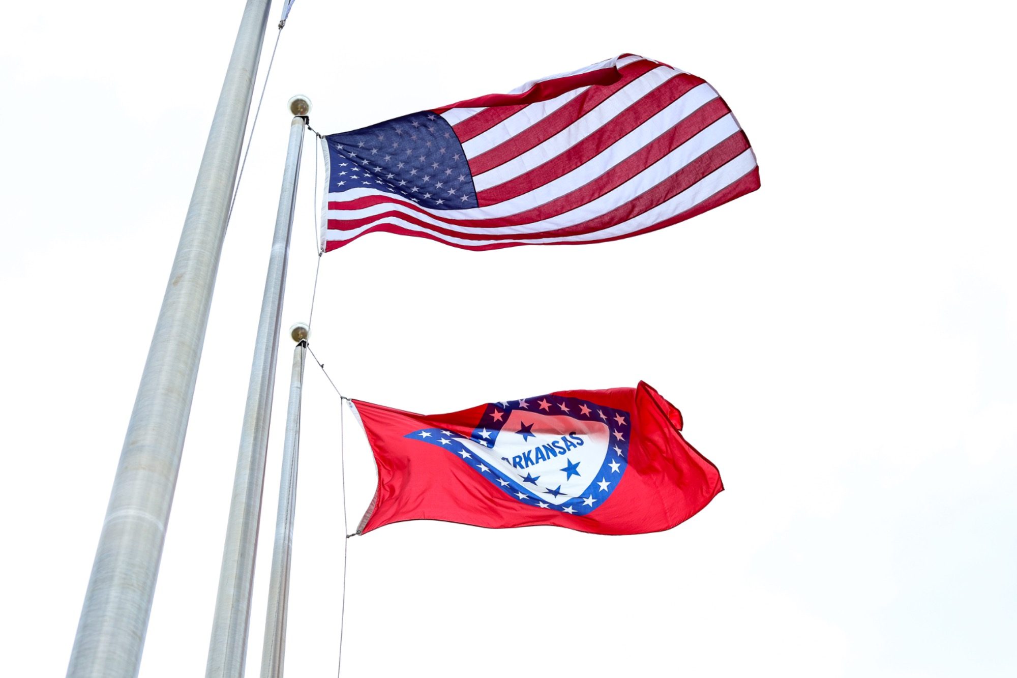 United States flag above Arkansas state flag against a cloudy sky.